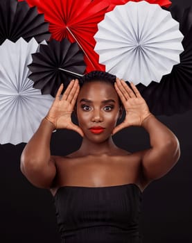 Black woman, origami fans and hand with makeup for skin glow or shine with creative artwork isolated in dark background. African female person or model and traditional oriental art with fashion.