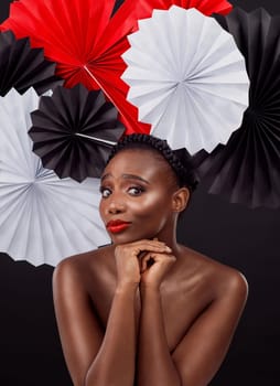 Woman, portrait and beauty with origami fans in studio isolated on a dark background. Face, makeup cosmetics and skincare of black female model with traditional Japanese paper art for geisha hat.