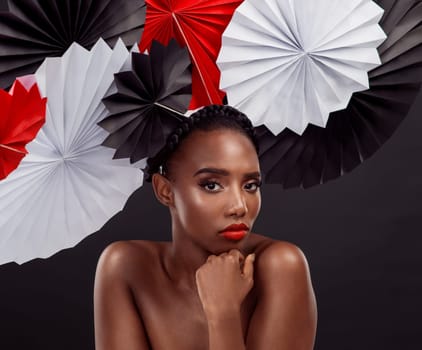 Woman, portrait and beauty with origami fans in studio isolated on a dark background. Face, makeup cosmetics and skincare of black female model with traditional Japanese paper art for culture hat.