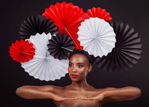 Woman, beauty and hand with origami fans in studio isolated on a dark background. Face, makeup cosmetics and skincare of black female model with traditional craft paper art for cultural geisha hat.