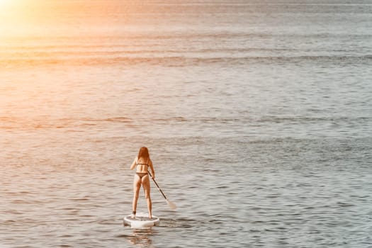 Sea woman sup. A happy positive woman in hat with family relaxing in sea, aerial back view of family on SUP board floating on calm water. Active lifestyle at sea. Summer vacation. Slow motion