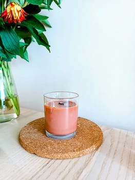 Handmade soy organic eco brown candle with wooden stick staying on the wooden table with flowers. High quality photo. Morning routine. Morning rituals. Meditations