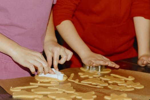 Two unrecognizable Caucasian girls stand at the table and together cut out a form of dough on baking paper in a baking tray, close-up side view. Step by step instructions. Step 21