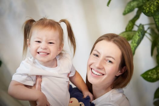 Happy loving family. Mother and daughter child girl playing and hugging in living room with wicker chair