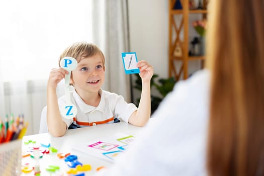 Smiling boy holding alphabet flashcards in front of a woman. Education and learning concept with copy space for design and print.