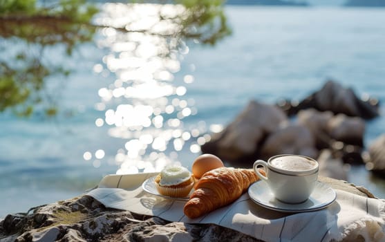 Peaceful breakfast setup with coffee and croissant on a lakeside rock, glistening water