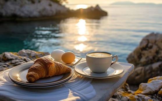 Peaceful breakfast setup with coffee and croissant on a lakeside rock, glistening water