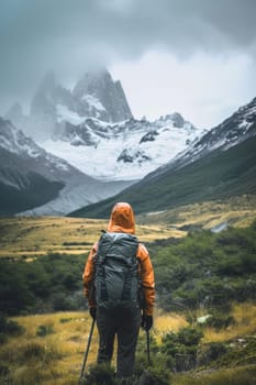 A hiker in orange jacket gazes at snowy mountains amidst greenery under a cloudy sky