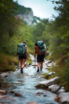 Two hikers with backpacks crossing a rocky stream in a forest, surrounded by autumn foliage