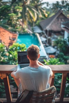 A relaxed individual working on a laptop with a scenic view of a resort pool and tropical greenery