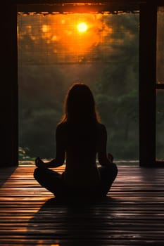 Silhouette of a woman practicing yoga during a tranquil sunset indoors