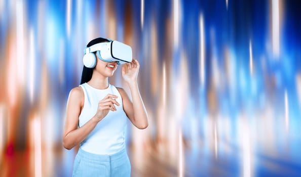 Female standing and wearing white VR headset and white sleeveless connect metaverse, future technology creating cyberspace community. She enjoy look fantasy abstract light around her. Hallucination.