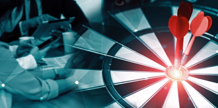 Business Target Goal For Success Strategy Concept - Red dart arrow hitting center goal on dart board with business people working in background showing precision and success of business target. uds