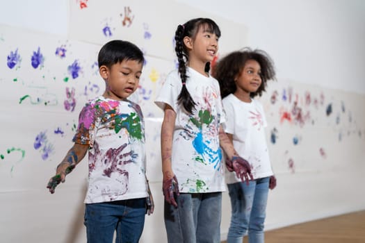 The student of school in white shirt learning drawing class. The little artists use their hand paint wall with print of their hand. The white shirt and wall colorful with stained colors. Erudition.