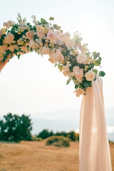 Corner of a wedding arch decorated with flowers and fabric standing in a clearing. High quality photo