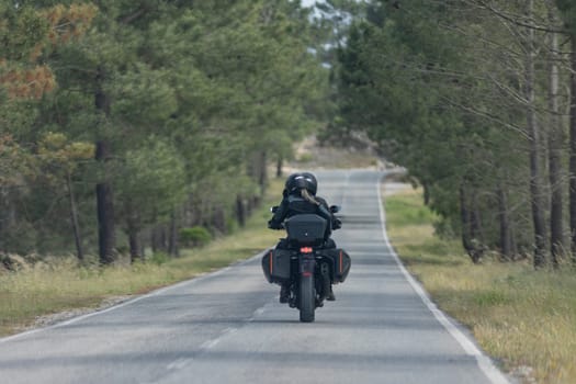 A man and woman are riding a motorcycle down a country road. The man is wearing a helmet and the woman is wearing a black jacket. The road is lined with trees, creating a peaceful