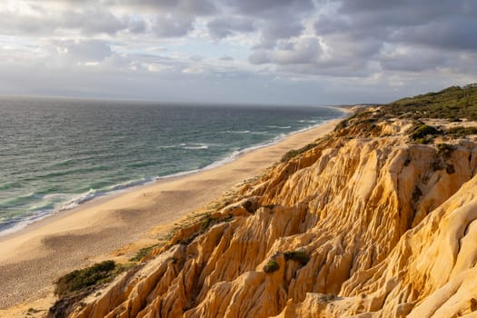 A beautiful beach with a rocky cliff in the background. The ocean is calm and the sky is cloudy