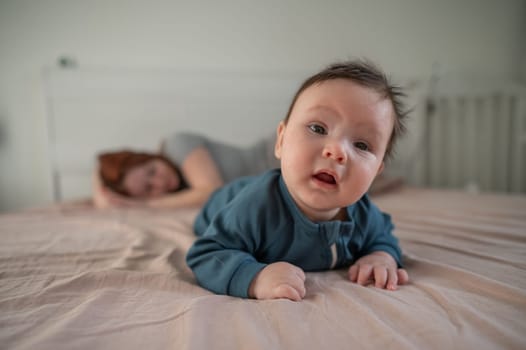 A three-month-old boy lies on his stomach on the bed and his mother sleeps behind him. Postpartum depression