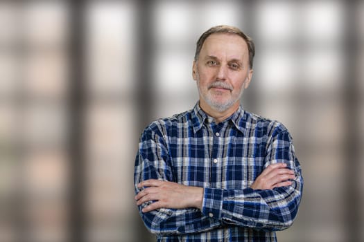 Portrait of a handsome mature man with folded arms standing in office. Checkered windows background.