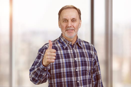 Smiling confident mature man giving his thumb up. Okay gesture sign. Office windows background.