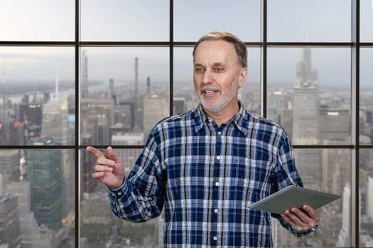 Happy cheerful aged man with tablet pc. Checkered windows background with cityscape view.