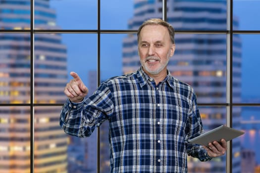 Portrait of cheerful aged man with tablet pc. Checkered night cityscape background.