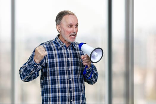 Portrait of confident elderly mature business man giving a speech in megaphone. Blurred windows background.