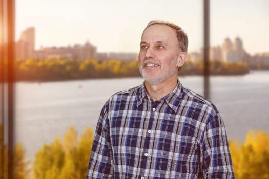 Portrait of happy cheerful caucasian man is looking up standing in office. River scape background.