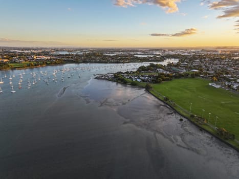 Drone shot of the Tamaki river with cloud reflections at sunset. Sailboats on moorings line up the river and marina in New Zealand