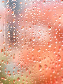 Closeup of raindrops on a window, showcasing the fluidity and beauty of water, with tints of orange and shades of moisture in the droplets of drizzle