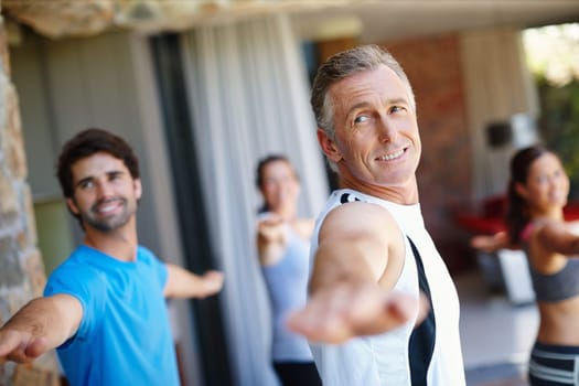 Mature man, pose and happy in yoga class for fitness and mental wellbeing, workout and daily lesson to coach people. Male yogini, warrior posture and yogis or students practice strength and balance
