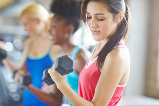 Woman, dumbbell and gym class in group or weightlifting workout for bicep growth or muscle, arms or strong. Female person, friends and smile for fitness training at wellness club, health or goals.