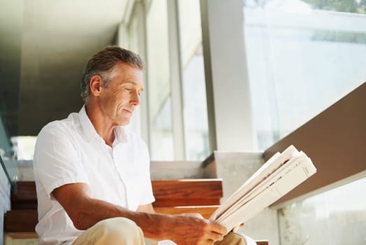 Old man, reading and newspaper in home or article for global current events, stock market or journalism. Male person, stairs and press information with opinion report in living room, relax or review.