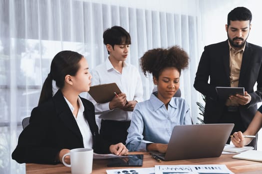 Multiracial analyst team use BI dashboard data to analyze financial report on meeting table. Group of diverse business people utilize data analysis by FIntech for success business marketing. Concord