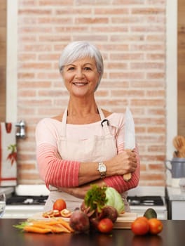 Senior woman and cooking with knife in kitchen or confident, tomato or carrots for diet. Female chef or portrait with healthy vegetables for nutrition, green lettuce and onion in retirement home.