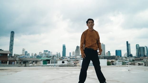 Motion shot of B-boy dance performance by professional street dancer at rooftop with sky scrapper, city view. Attractive asian hipster show energetic footstep. Outdoor sport 2024. Endeavor.