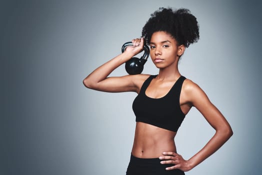 Portrait, black woman and workout with kettle bell in studio on grey background to exercise for health or fitness. Female person, confident and weights for gym or training, wellbeing and wellness.