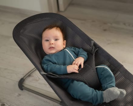 Cute newborn baby dressed in blue overalls sitting in a baby lounger