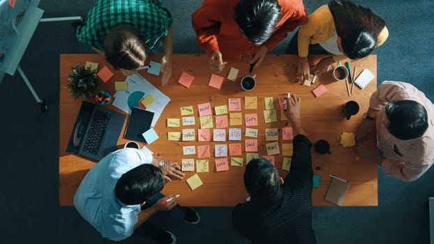 Top view of smart diverse business team working together and clapping hand while brainstorming marketing idea or creative startup project by using sticky notes and stick at meeting table. Convocation.