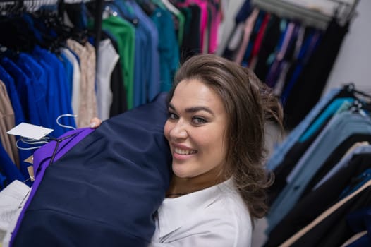 Top view of a chubby-cheeked woman holding an armful of clothes in a plus size store
