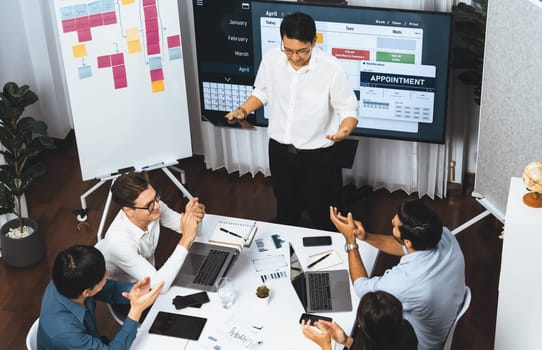 Project manager communicate and collaborate with team using project management software display on monitor, tracking progress of project task and making schedule plan at meeting table. Prudent