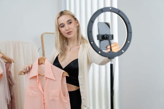 Young social medial content creator woman make fashion video. Blogger smiles to camera and light ring while making persuasive online clothing sell vlog to audience or follower. Blithe