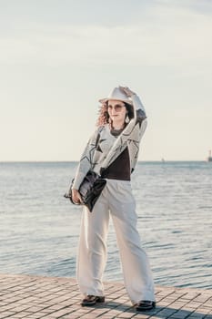 Stylish seashore woman. Fashionable woman in a white hat, white trousers and a light sweater with a black pattern on the background of the sea