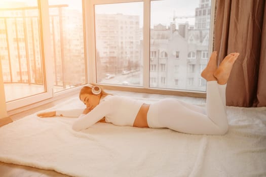 Side view portrait of relaxed woman listening to music with headphones lying on carpet at home. She is dressed in a white tracksuit