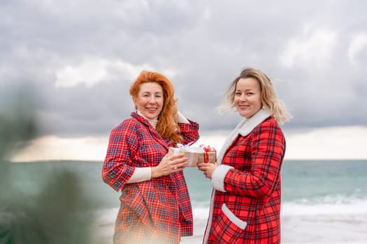 Sea two Lady in plaid shirt with a christmas tree in her hands enjoys beach. Coastal area. Christmas, New Year holidays concep.