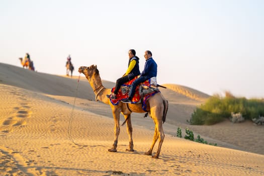 Jaisalmer, Rajasthan, India - 25th Dec 2023: Young couple tourists sitting on camel enjoying the walk sand dunes in sam or dubai