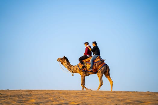 Jaisalmer, Rajasthan, India - 25th Dec 2023: Young couple tourists sitting on camel enjoying the walk sand dunes in sam or dubai