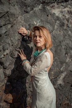 Middle aged woman looks good with blond hair, boho style in white long dress on the beach decorations on her neck and arms