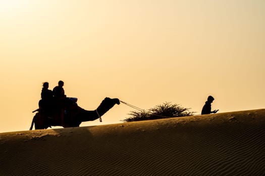 Silhouette of camel with two people sitting on it crossing over sand dunes in Sam Jaisalmer Rajasthan India