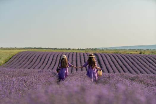 Mom and daughter are running through a lavender field dressed in purple dresses, long hair flowing and wearing hats. The field is full of purple flowers and the sky is clear